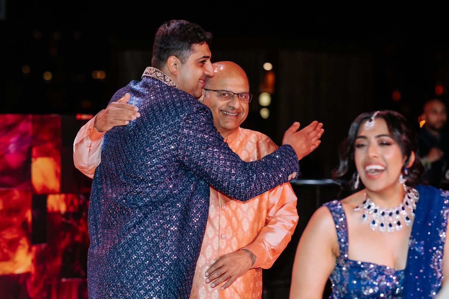 Groom in blue sherwani sharing warm embrace with elder at Indian wedding celebration.