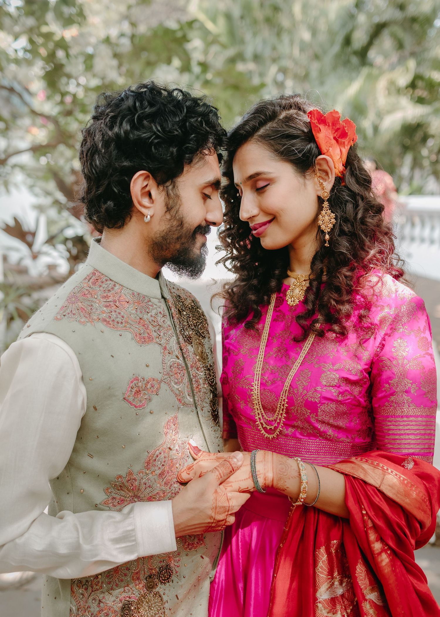 Couple in traditional Indian attire sharing a romantic moment, woman in pink saree with gold jewelry, man in embroidered sherwani.