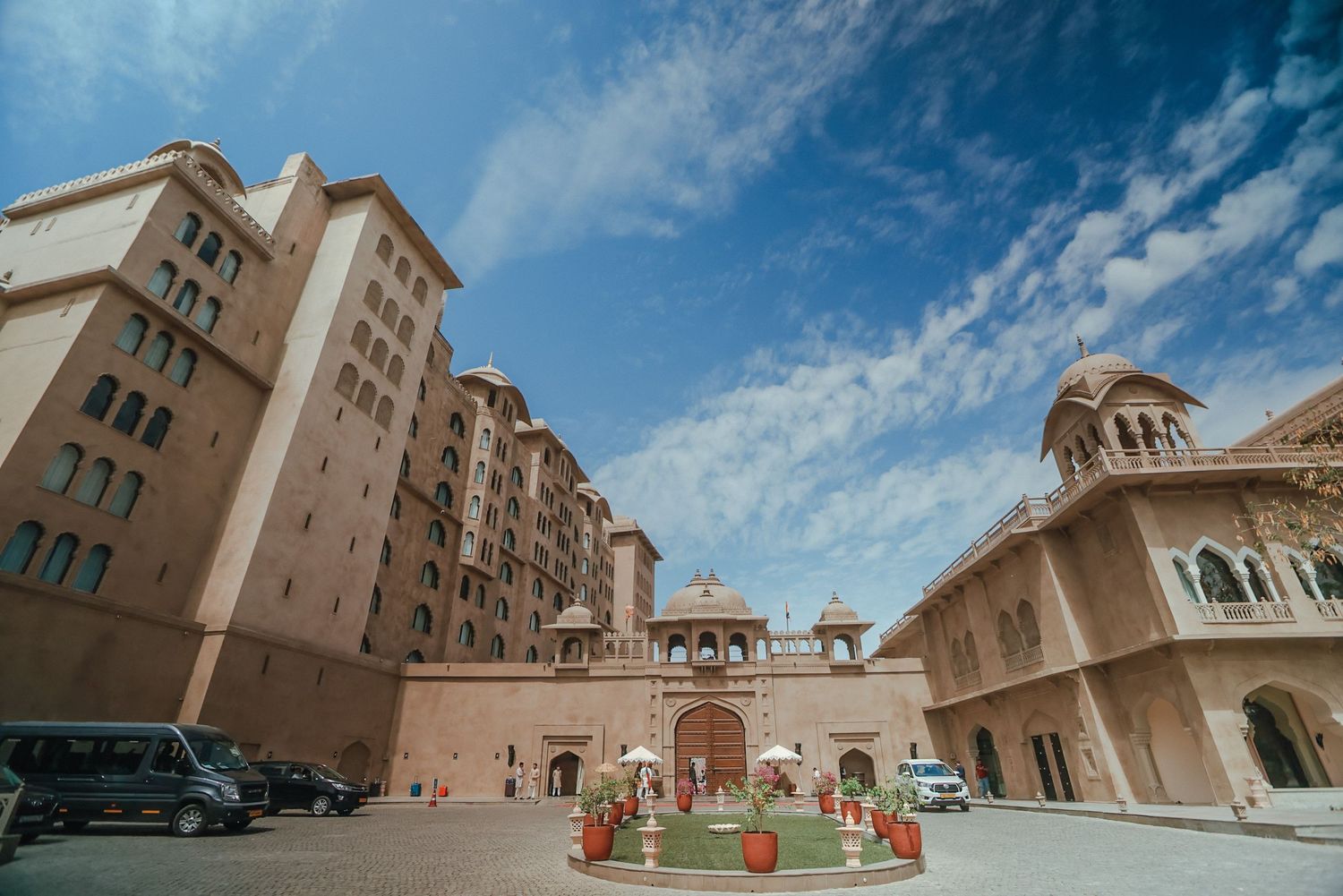Exterior view of a luxurious resort hotel with beige stone architecture and traditional domed towers against blue sky.