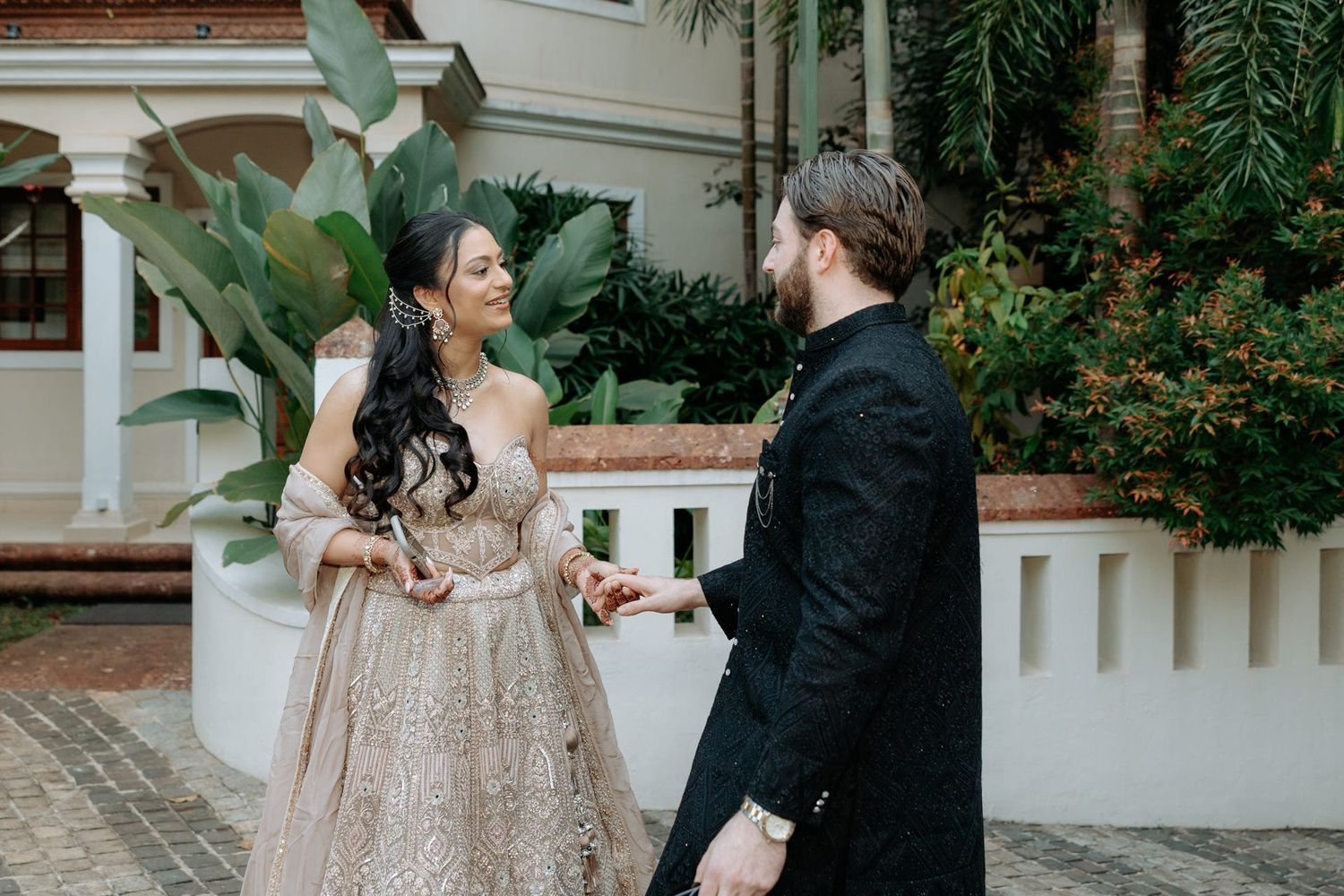 Couple in elegant wedding attire sharing a romantic moment outdoors, bride in champagne gown, groom in black suit.