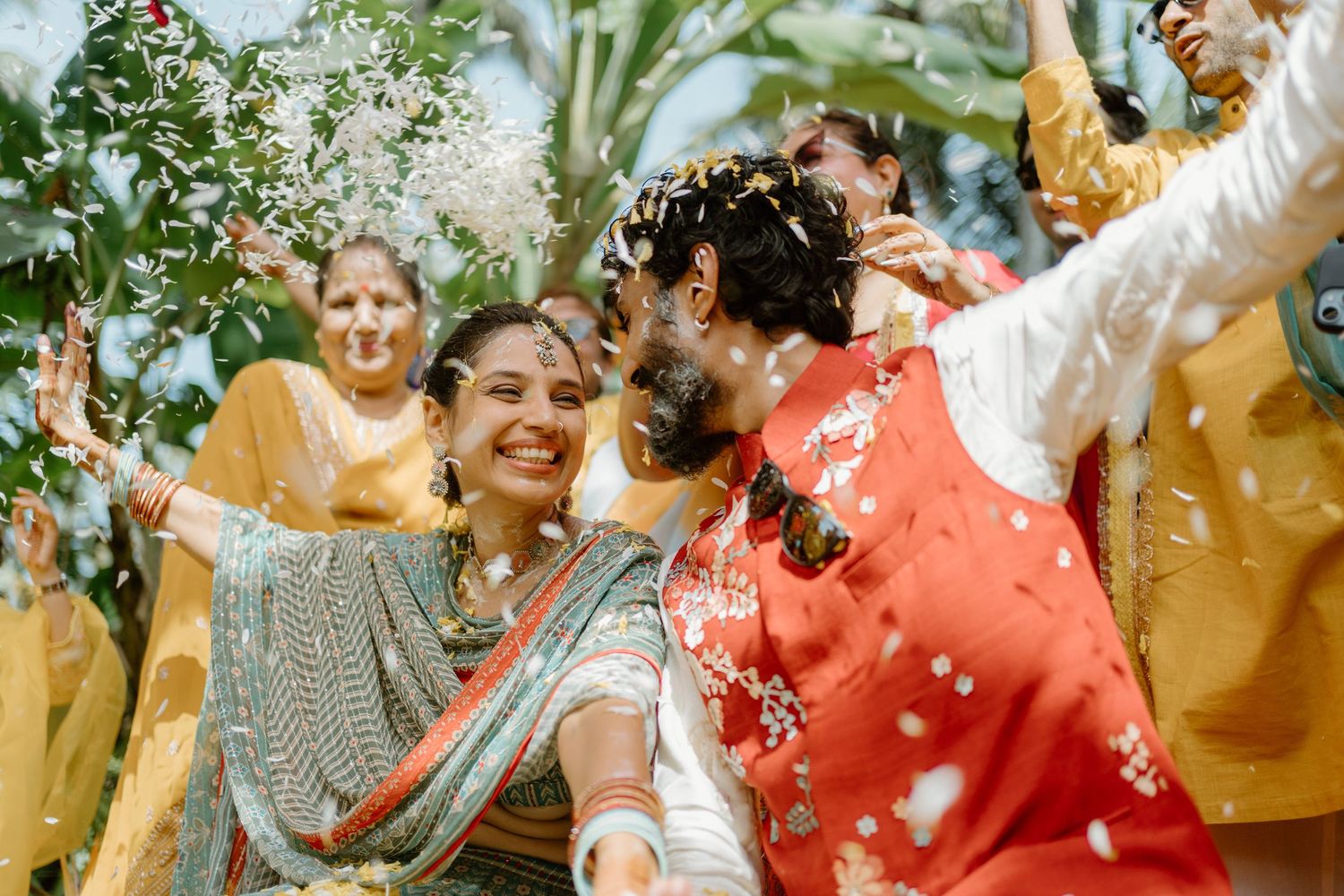 Indian bride and groom celebrate with flower petals during vibrant outdoor wedding ceremony.