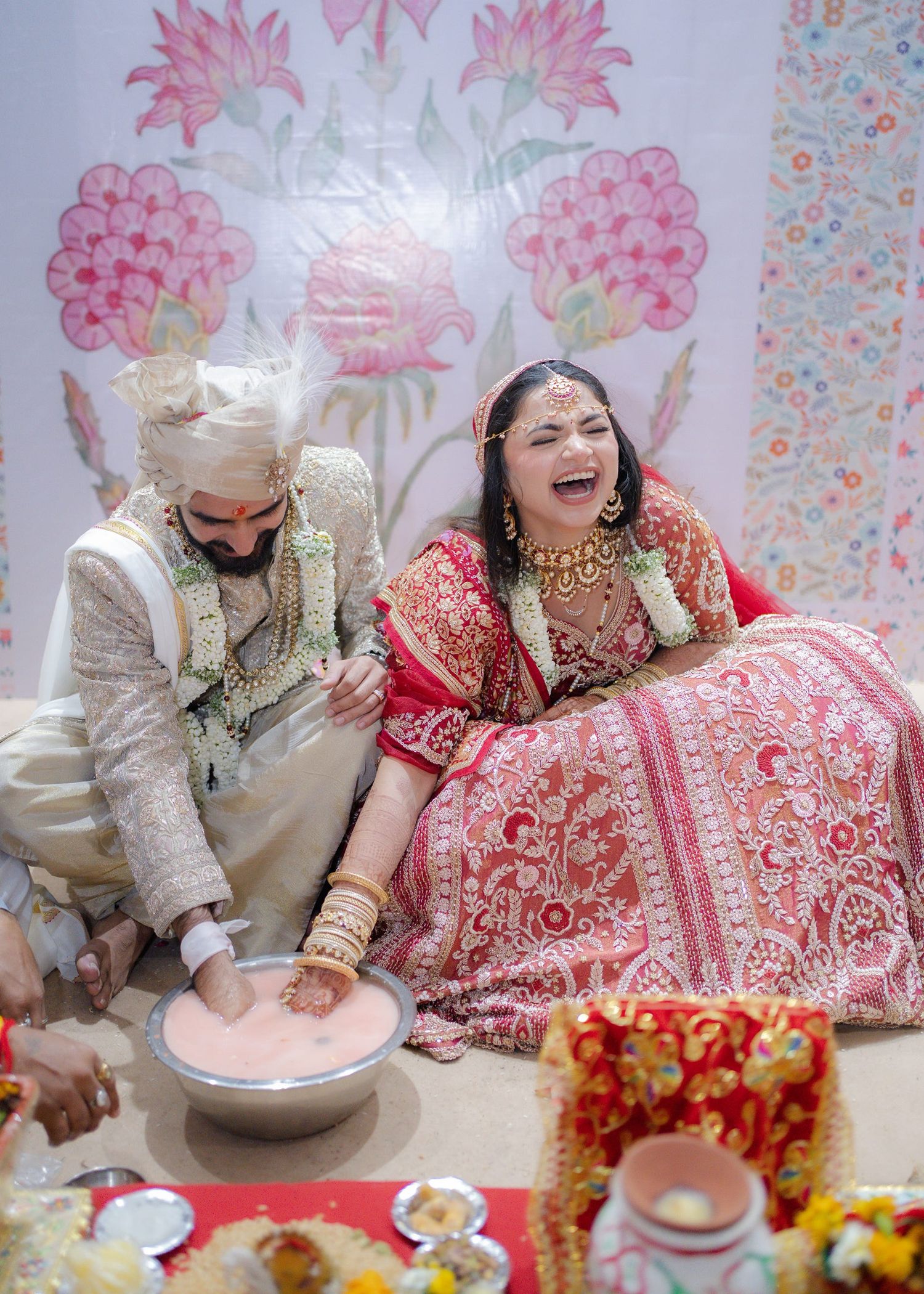 Joyful Indian bride in red lehenga and groom in white sherwani laughing during traditional Hindu wedding ceremony.