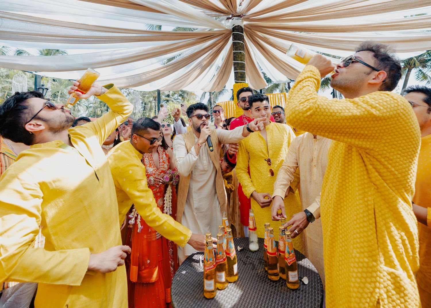 Celebrants in bright yellow outfits gather under a draped canopy during a festive party.