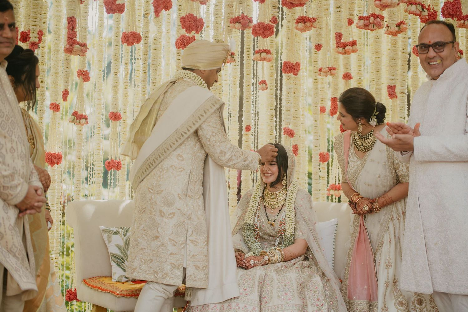 Traditional Indian wedding ceremony with white and gold decor featuring floral arrangements and elegant attire.