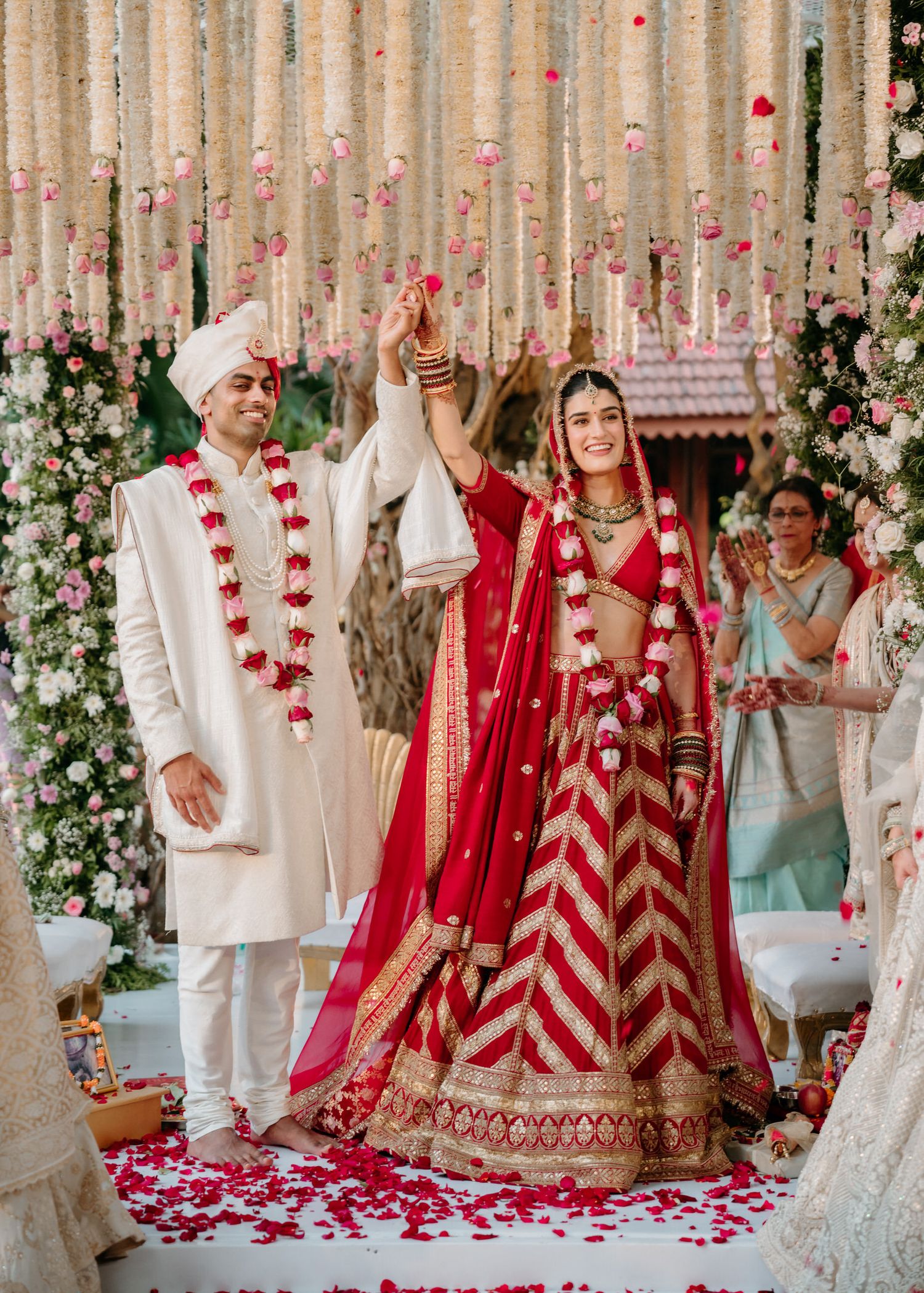 Traditional Indian wedding ceremony with couple in red and white attire under floral decor surrounded by rose petals.