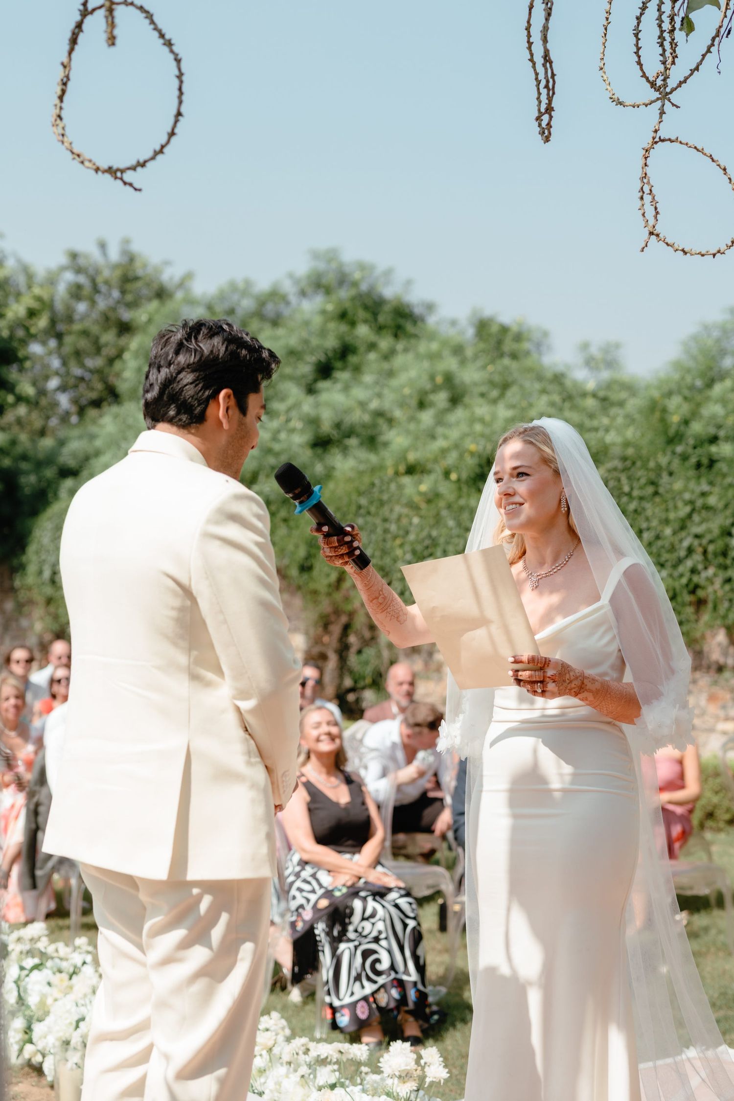 A couple exchanging vows during their outdoor wedding ceremony beneath a draped floral arch.