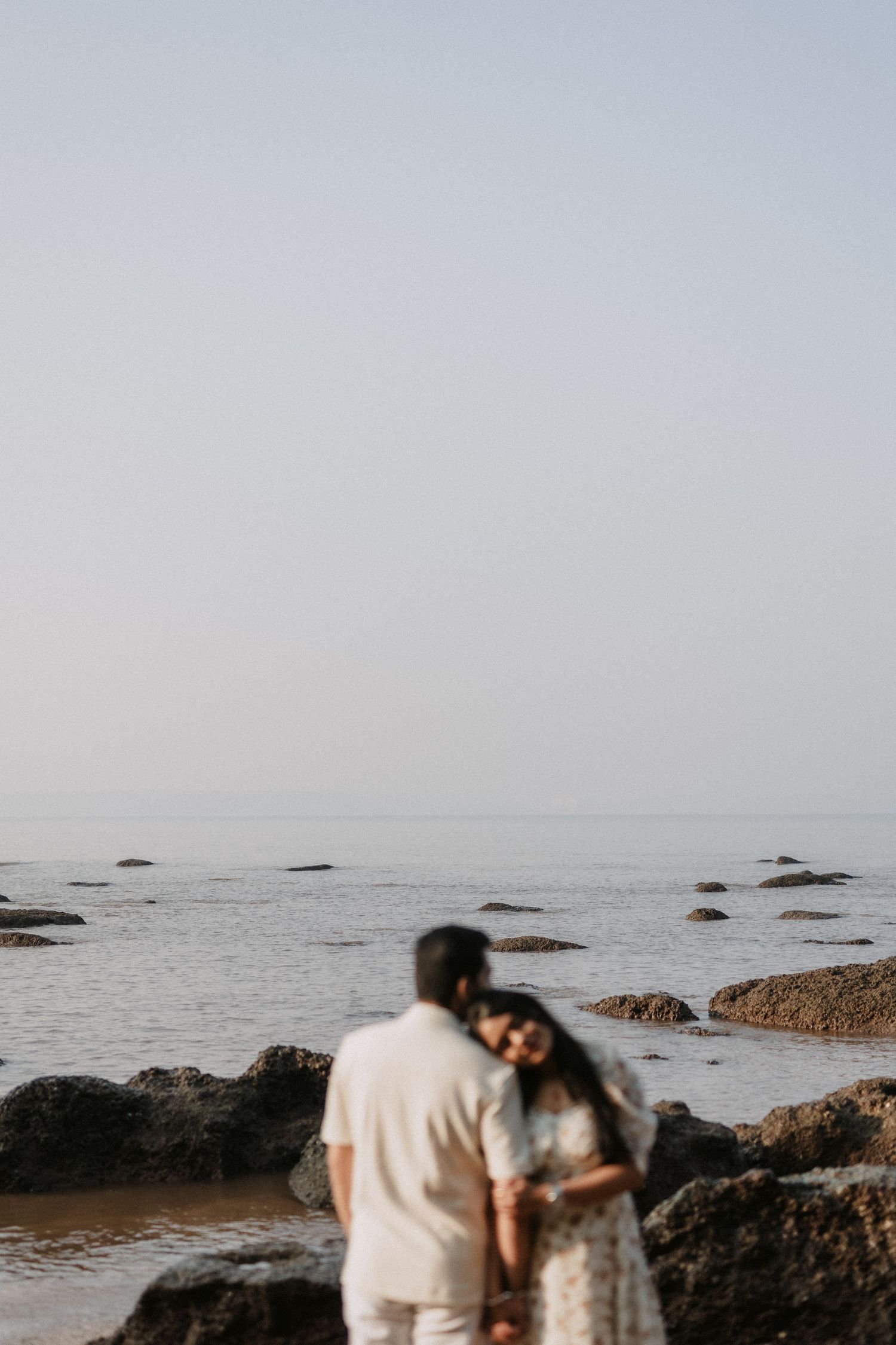 Romantic couple sharing a tender sunset moment on a rocky Goa beach with ocean waves in the background, captured by Studio RDP