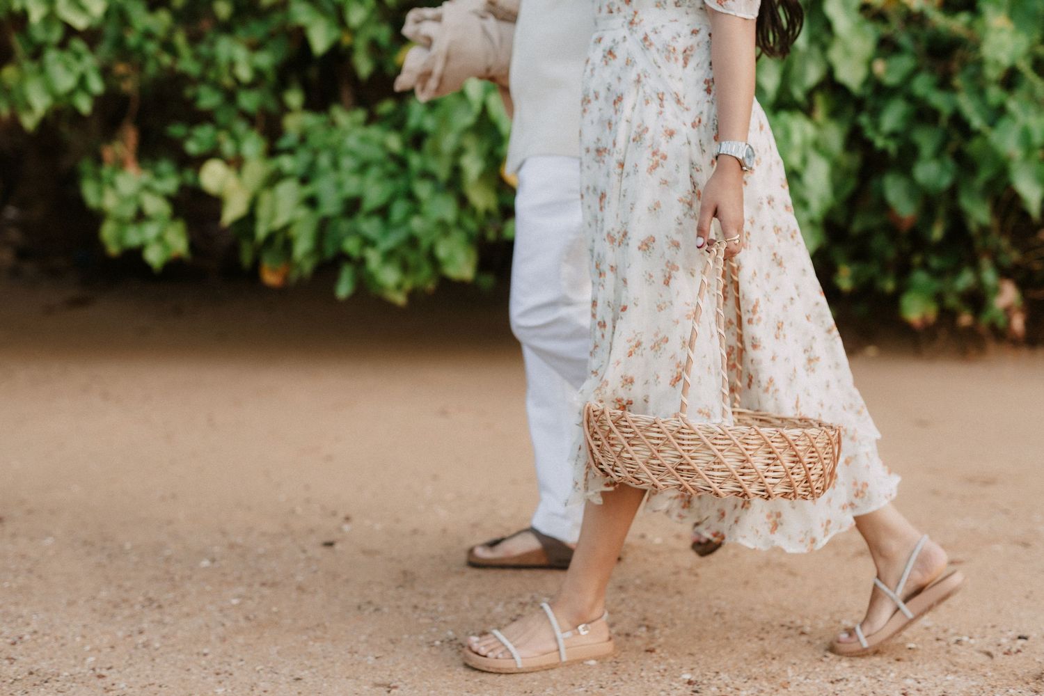 Several pairs of feet standing on a dirt ground wearing bohemian sandals and a lace dress visible in frame.
