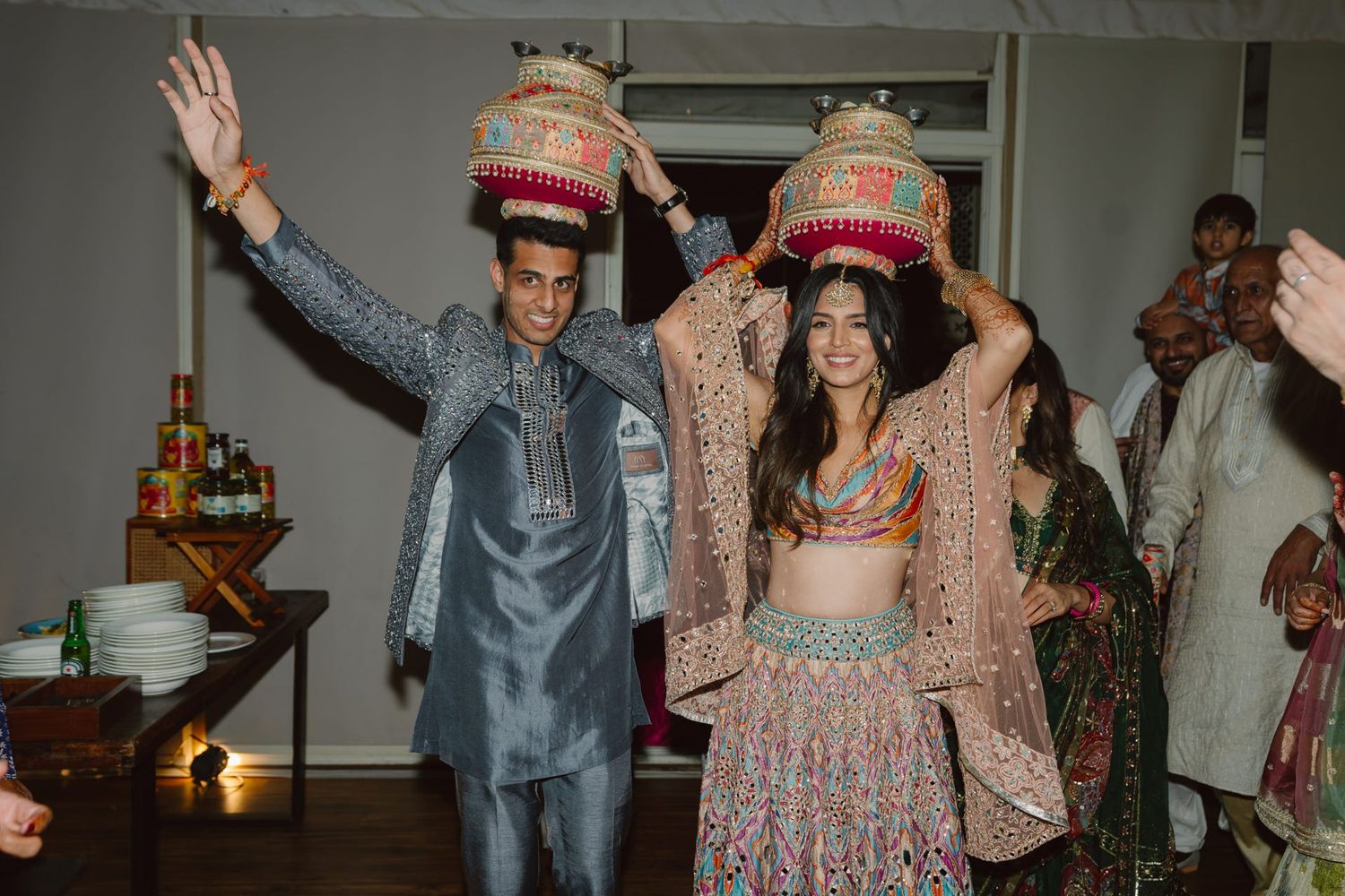 A couple balances decorative objects on their heads during a festive Indian wedding ritual.