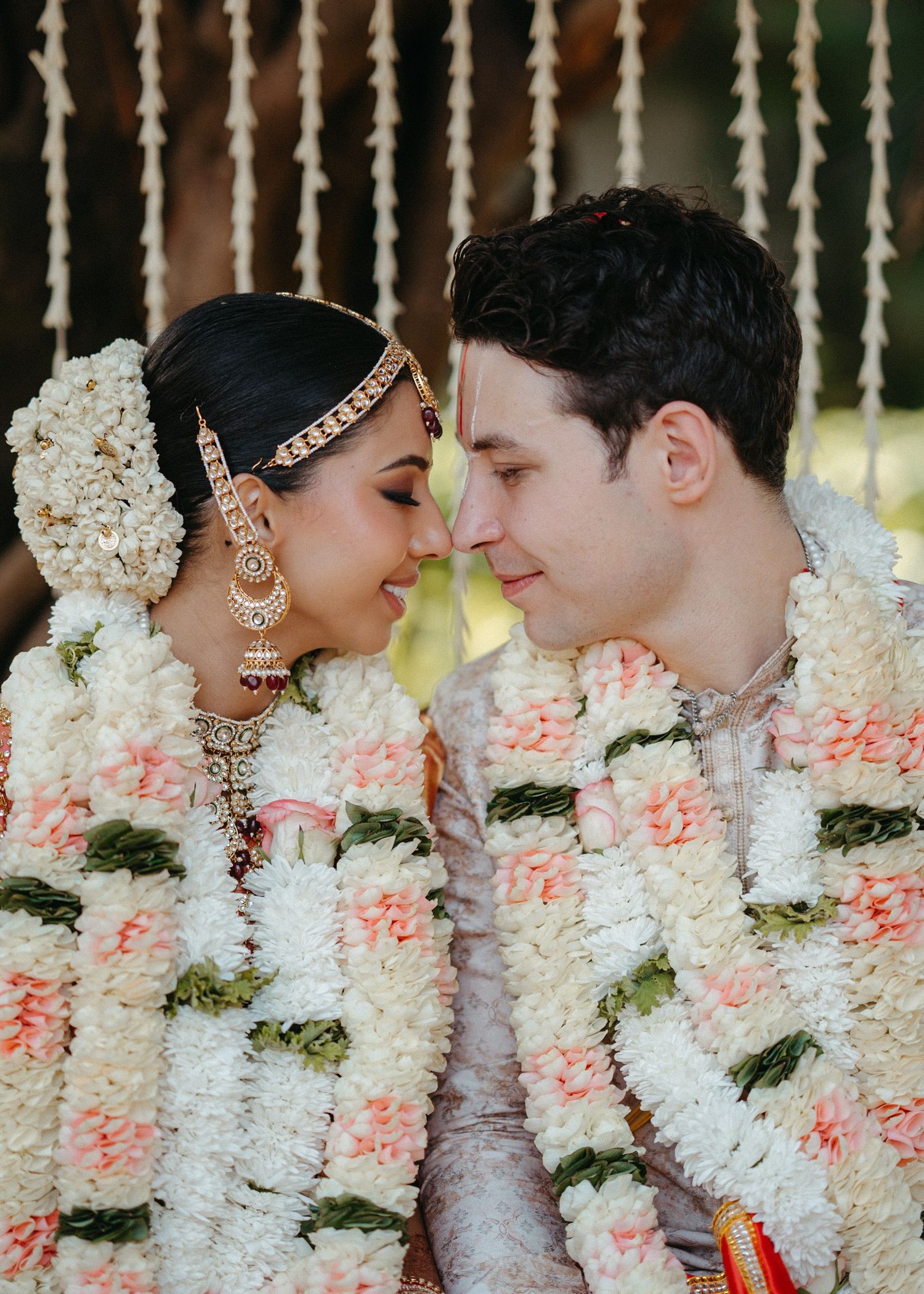 Close-up of a tender moment between newlyweds with hanging flower garlands.