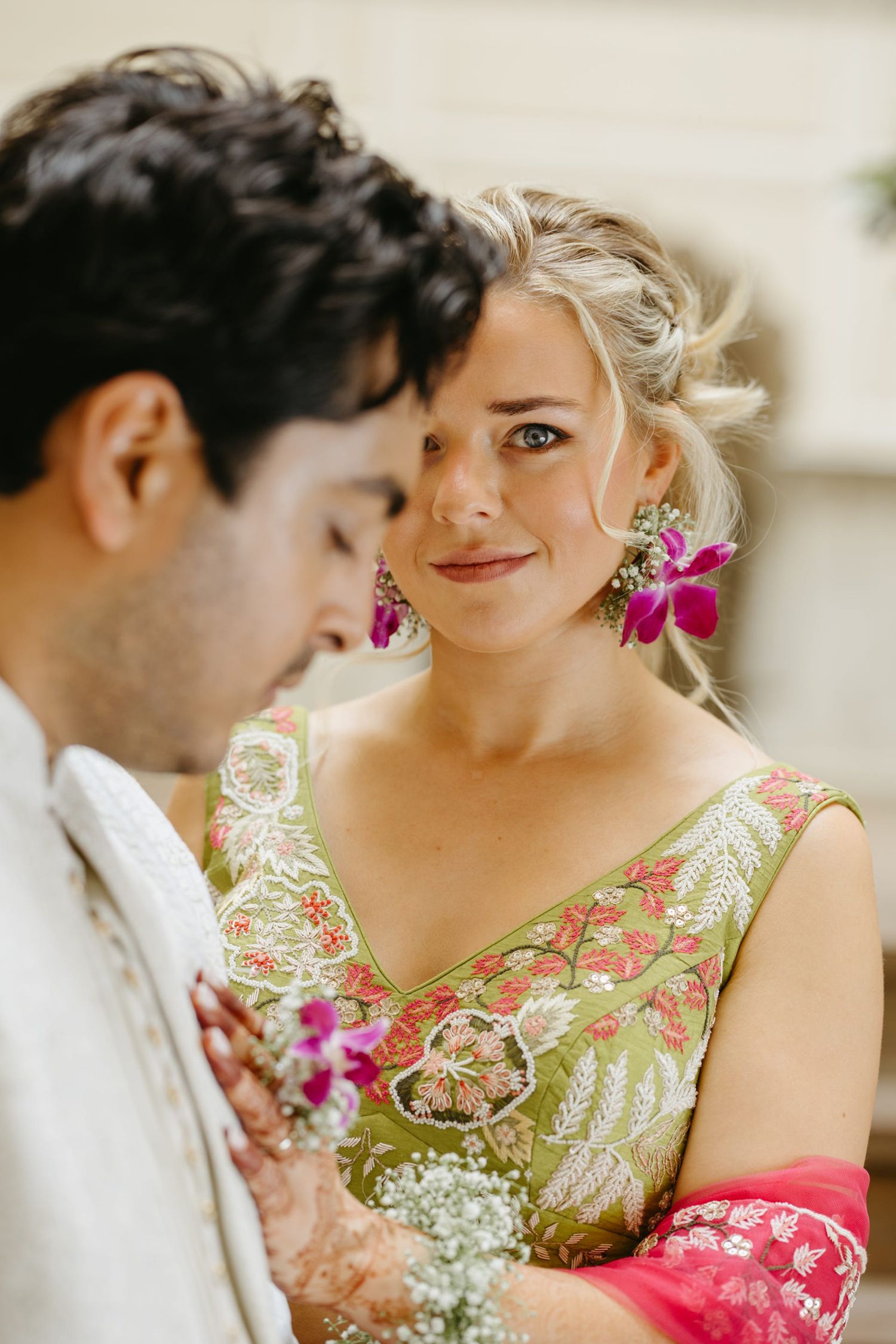 A couple in traditional fusion attire share intimate moments with pink floral accents.