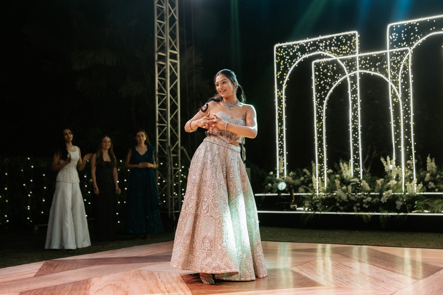 Elegant woman in embroidered gown performing on dance floor at glamorous wedding reception with arch lights.