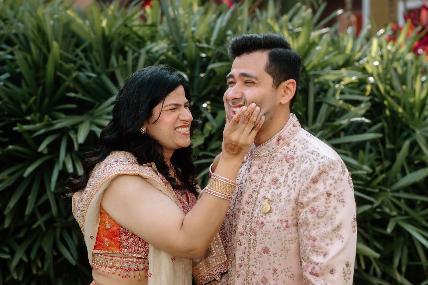 A couple shares joyful moments together in a garden setting with lush green plants in the background.