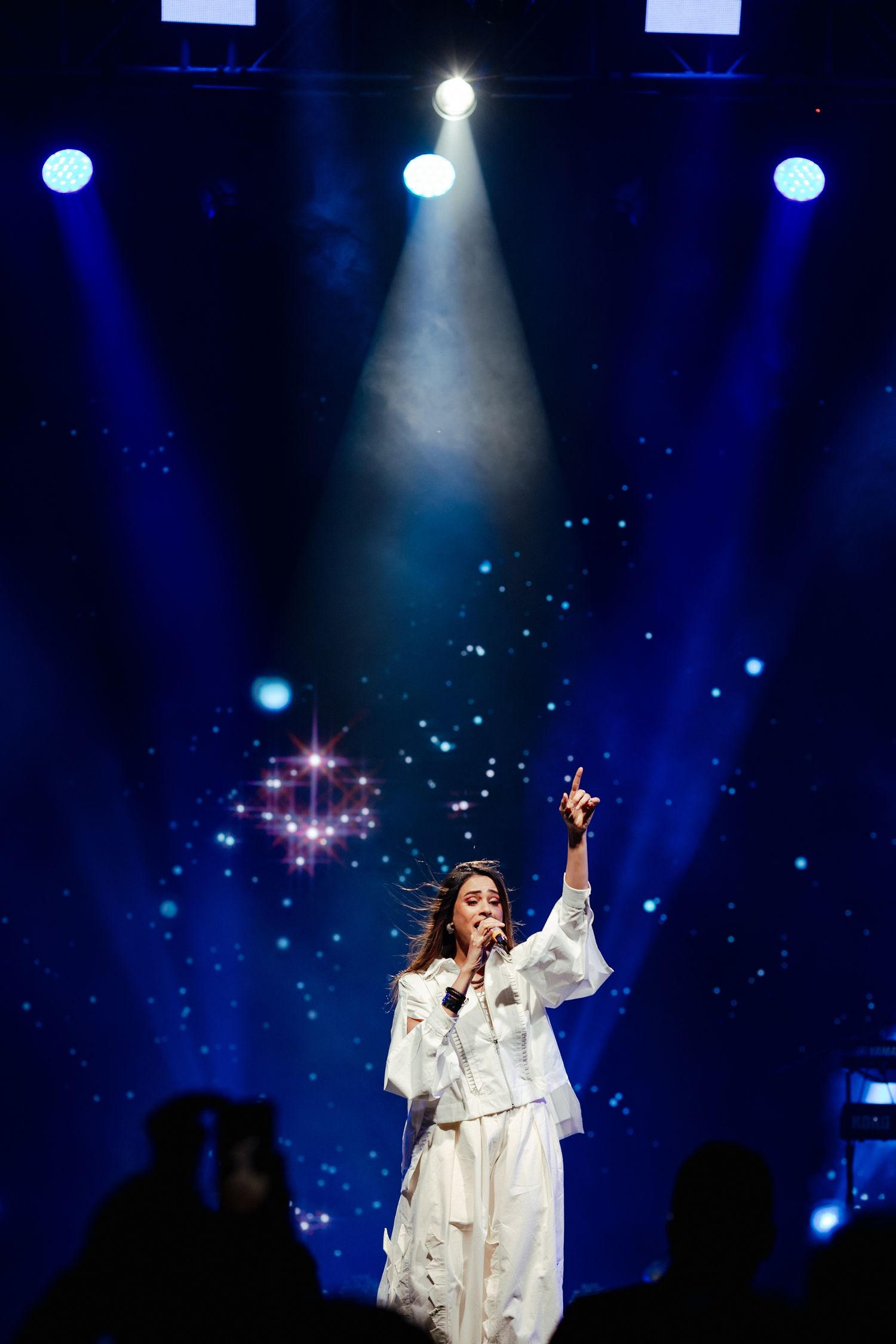 A performer in a flowing white gown stands on stage illuminated by dramatic blue spotlights during an evening concert.