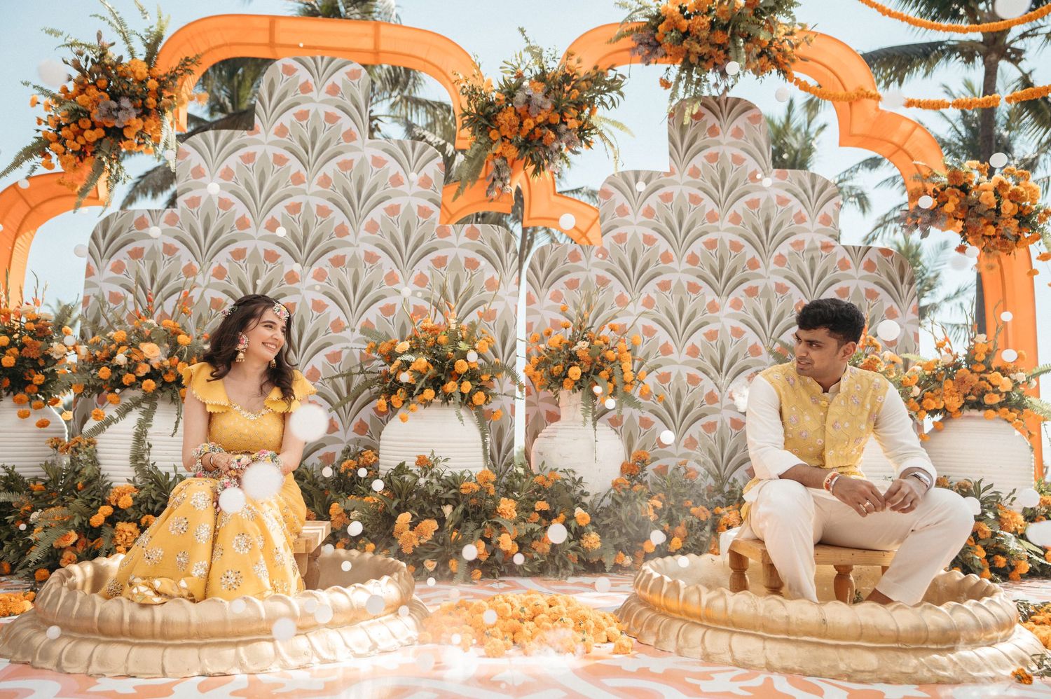 Elegant wedding event setup with orange floral arrangements, white decor and intricate patterned backdrop in rustic style.