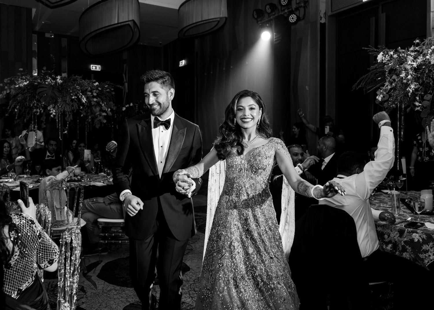 Black and white photo of a couple celebrating at a formal event wearing evening attire in a ballroom setting.