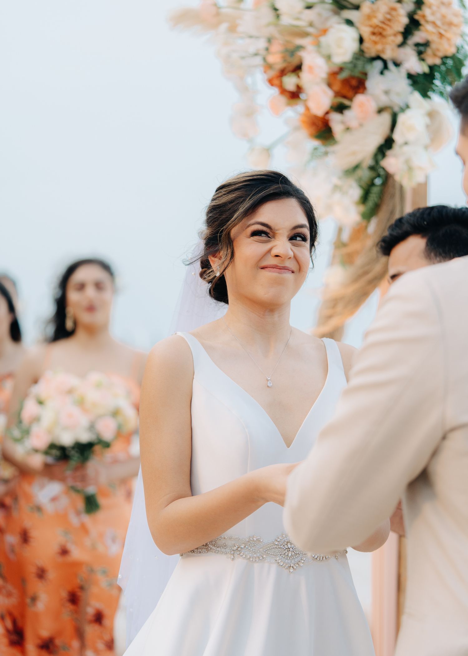 A wedding ceremony with a bride in a white V-neck dress with crystal belt details and floral arch decorations.