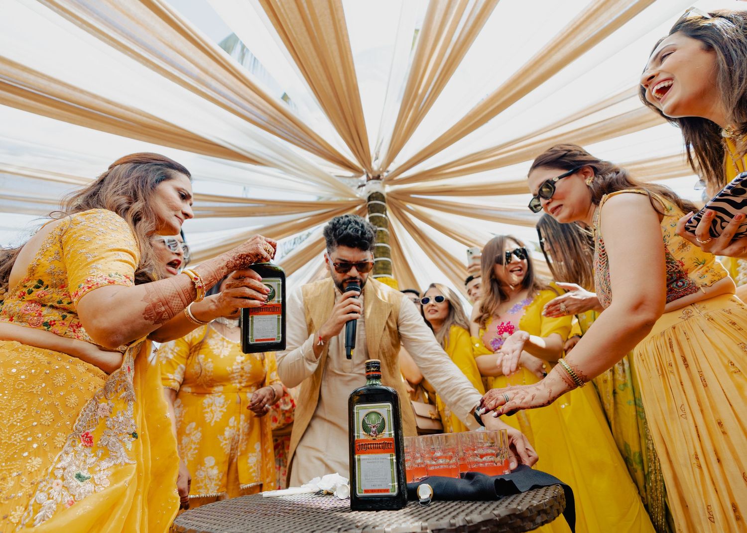 A group in yellow dresses gathers around a table with bottles during what appears to be a celebration.