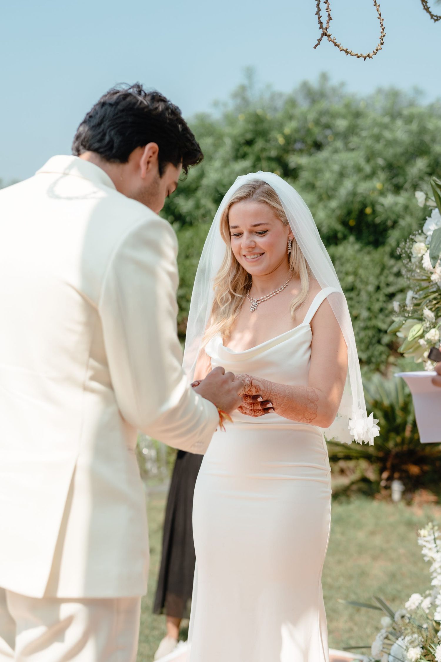 An intimate moment during a wedding ceremony as the couple exchanges rings under a floral-adorned arch.