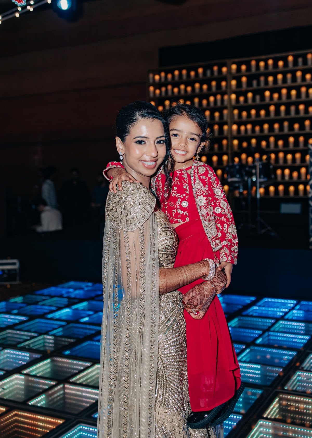 A couple in formal attire poses together against a dark backdrop with illuminated geometric patterns.