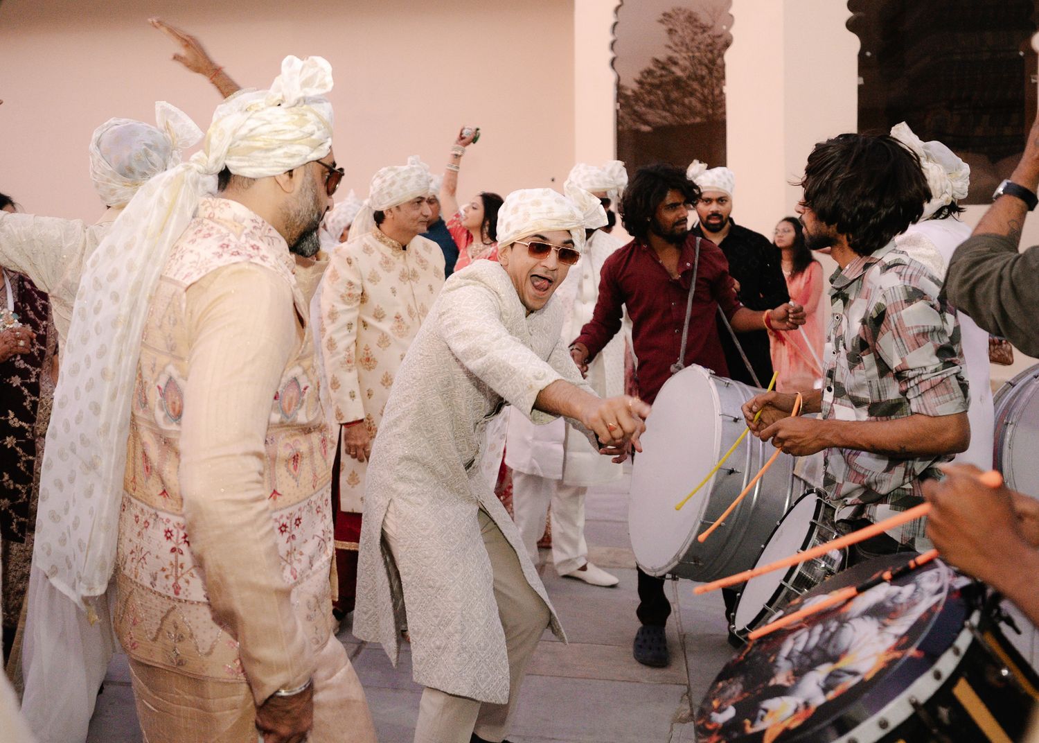Joyful Indian wedding baraat celebration with groom and guests dancing energetically with dhol drummers.