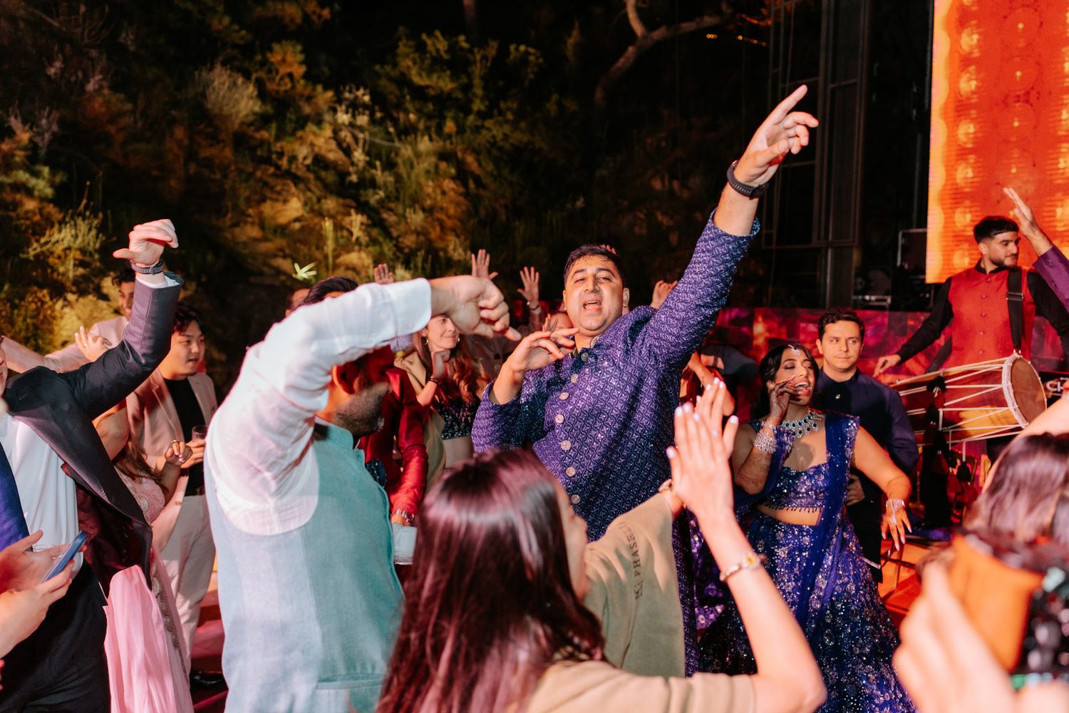 Guests dancing joyfully at a vibrant Indian wedding celebration outdoors at night.
