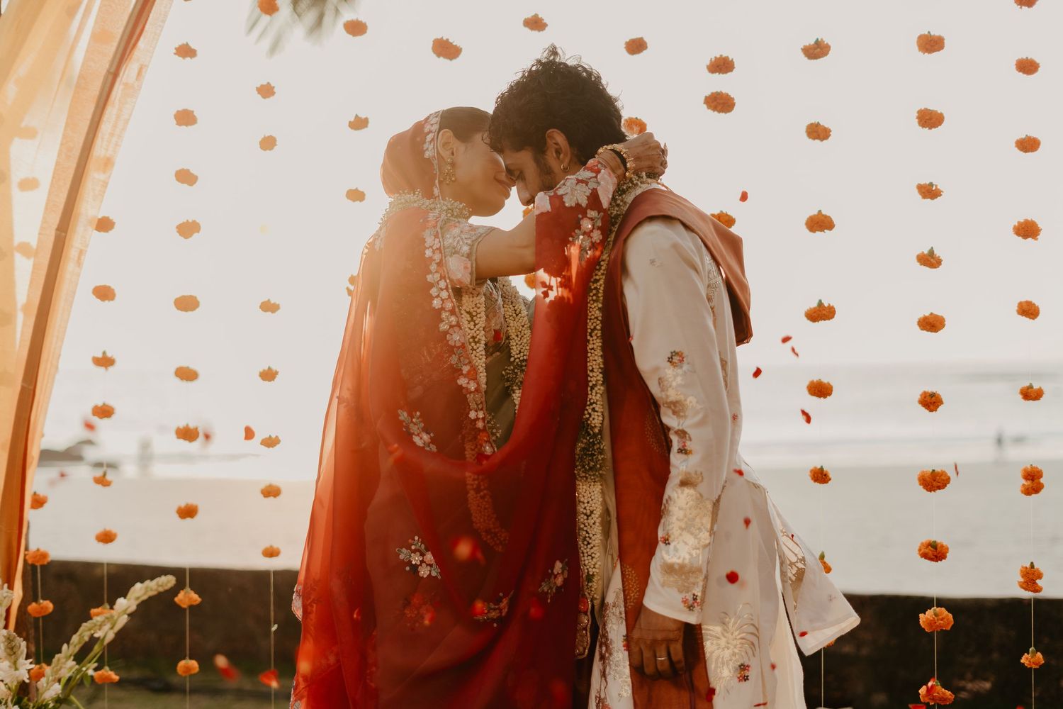 Indian couple in traditional wedding attire sharing a romantic moment under floral decorations.