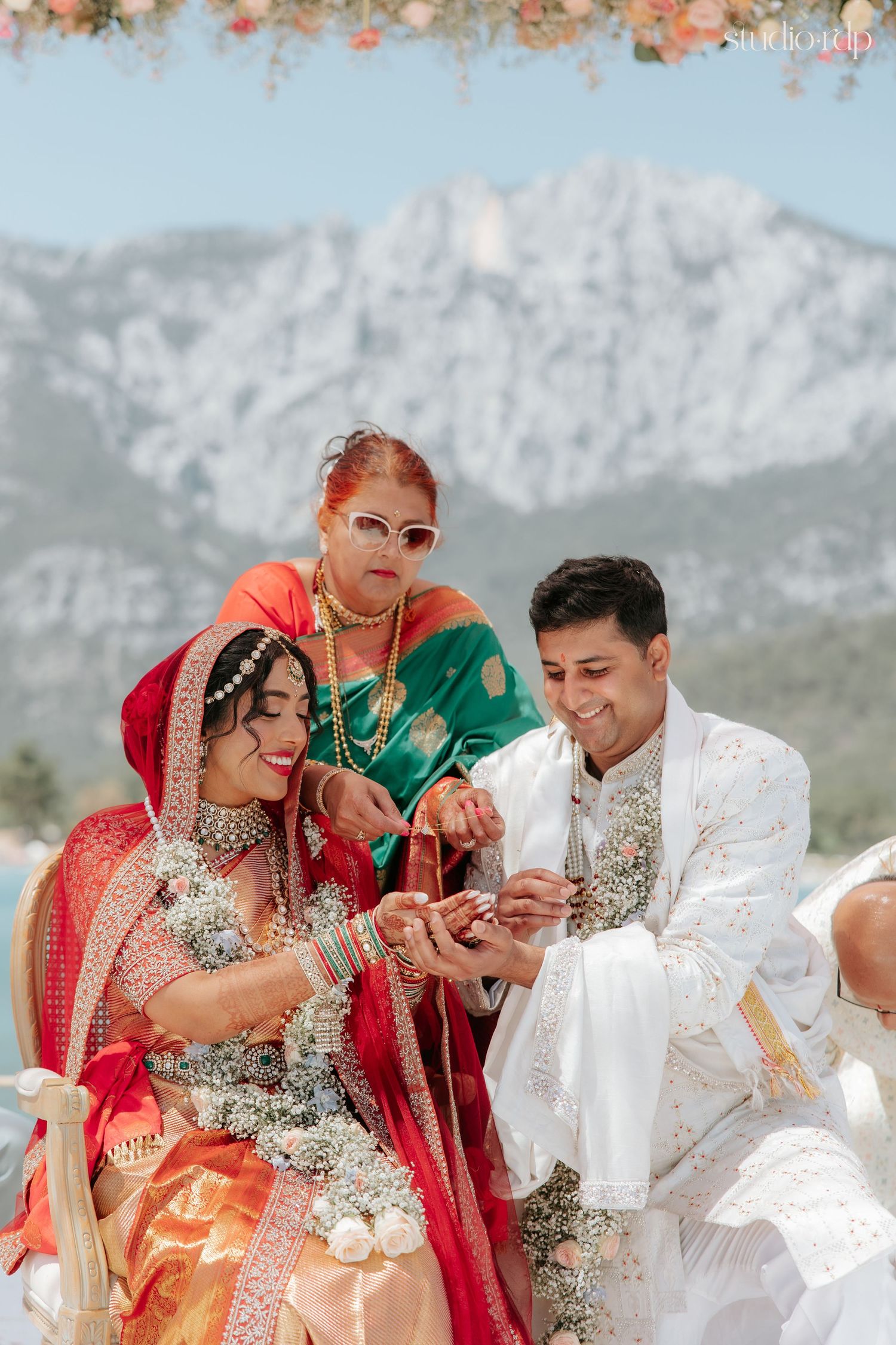 Indian bride and groom exchange rings during traditional Hindu wedding ceremony outdoors with mountain backdrop.