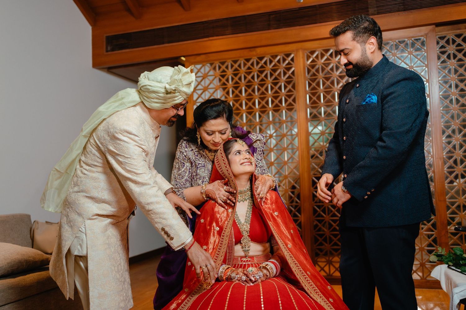 Bride in red lehenga getting ready with family assistance during traditional Indian wedding ceremony.
