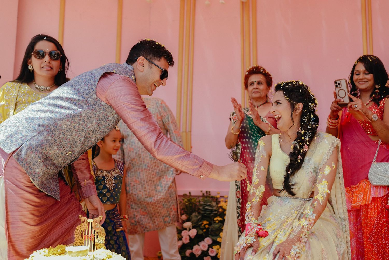 A festive moment at an Indian wedding ceremony with people in traditional attire celebrating a ritual indoors.