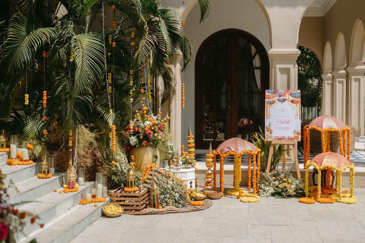 Elegant wedding reception decor features tropical palm leaves and golden lanterns along an outdoor covered walkway.