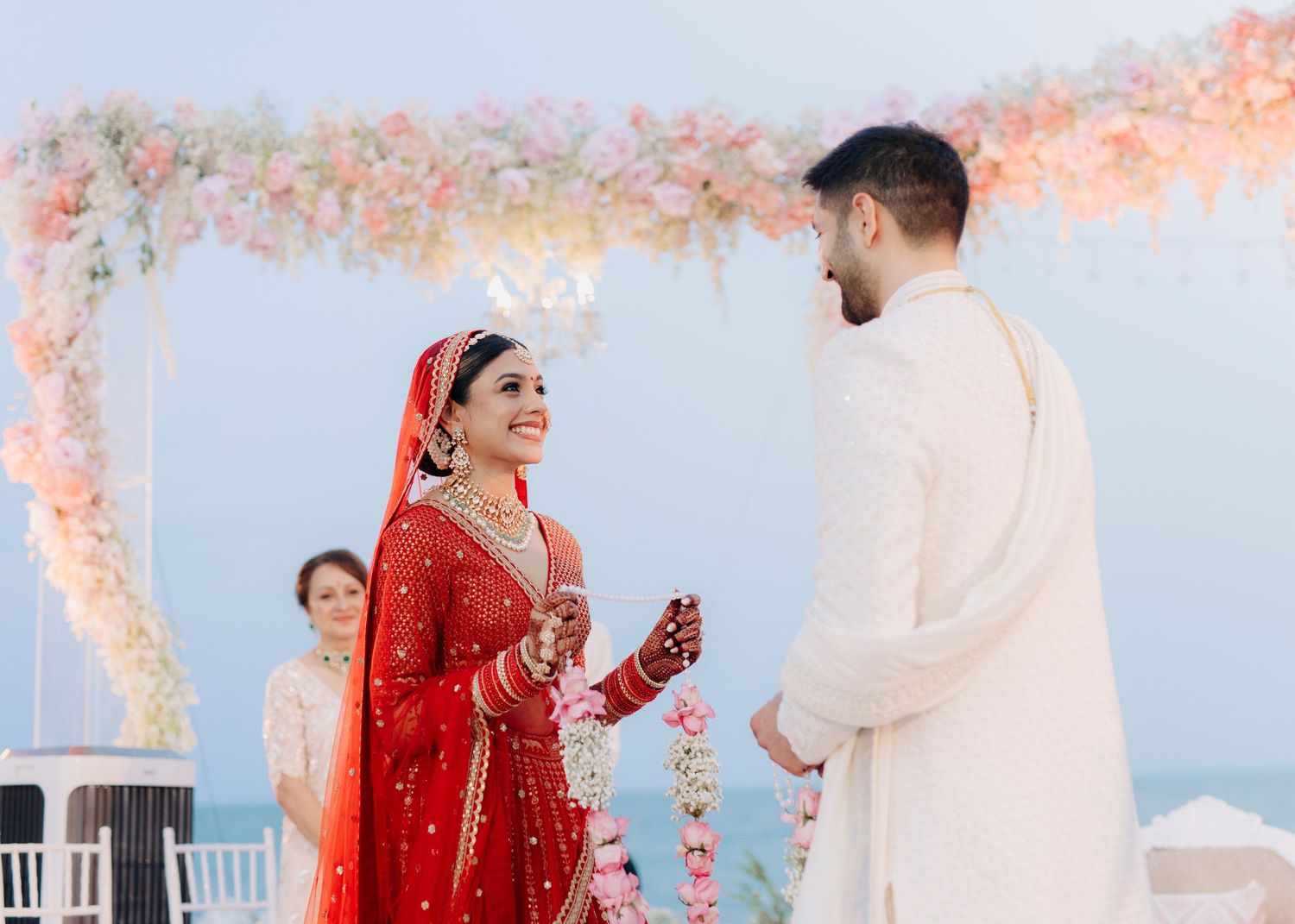 Traditional Indian wedding ceremony with a couple exchanging vows under a floral arch with pink blooms.