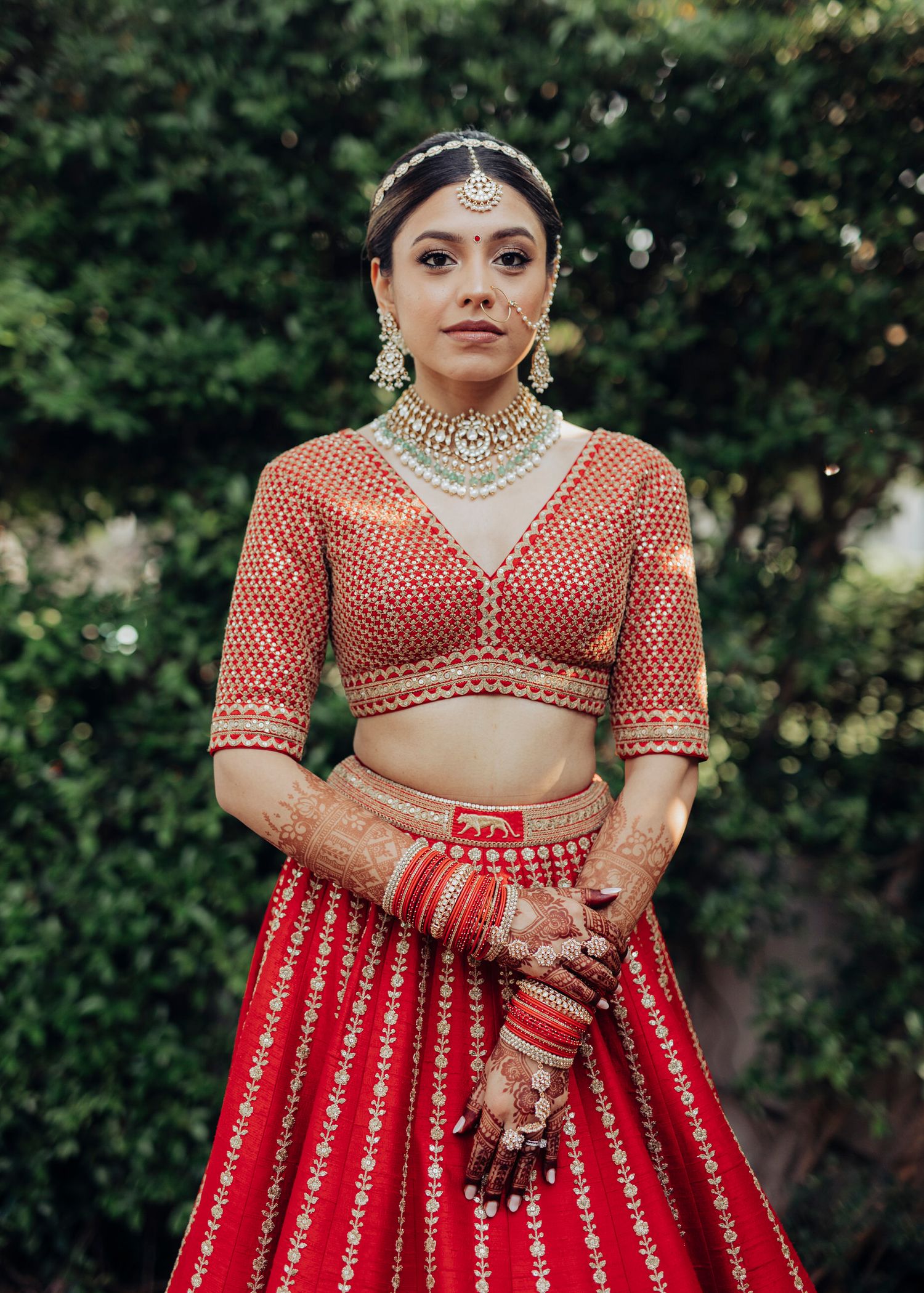 Traditional Indian bridal attire featuring a red and gold embroidered lehenga with matching crop top and ornate jewelry.