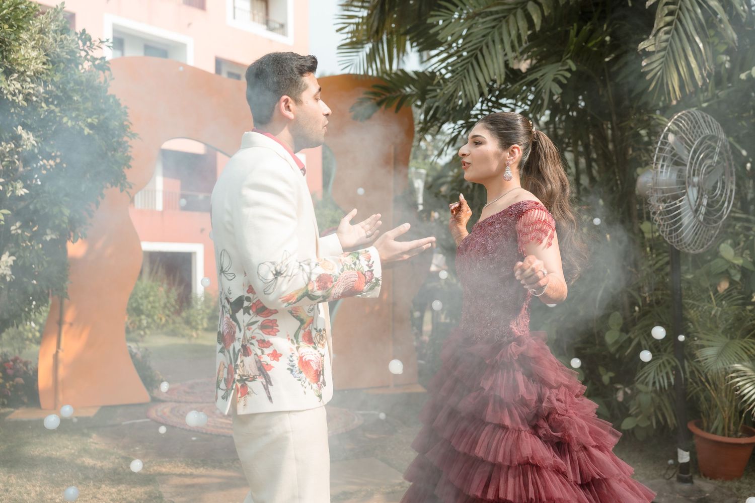 Romantic couple poses among palm trees with soft lighting and mist creating a dreamy atmosphere.