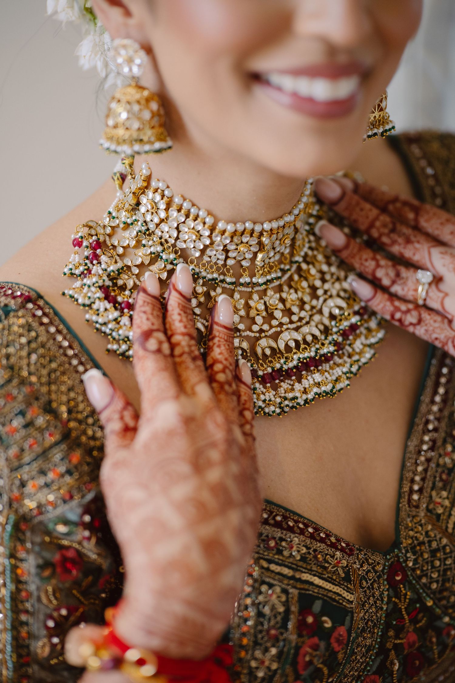 Close-up of ornate bridal jewelry and henna decorated hands on red and gold wedding attire.