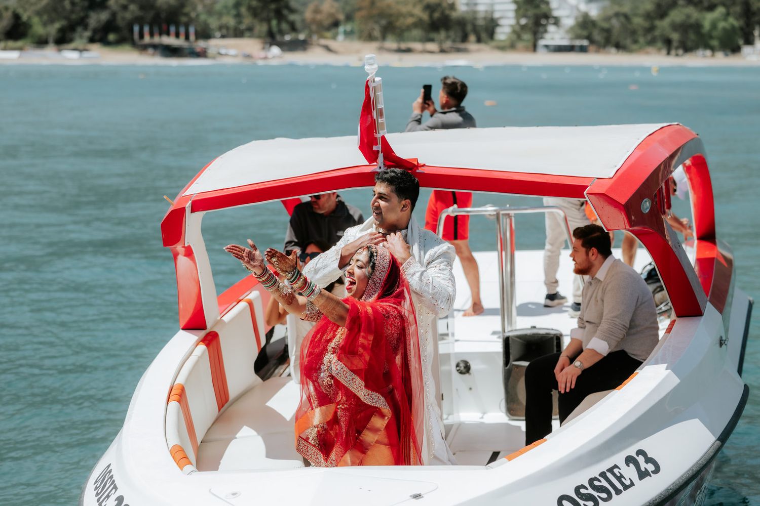 Indian bride in red saree and groom sit on a red and white speedboat Ossie 23 during a scenic wedding boat ceremony.