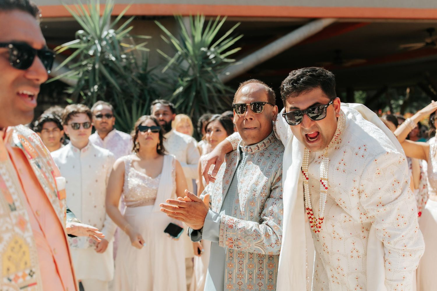 Guests in traditional Indian attire celebrate outdoors at a wedding ceremony with joy.