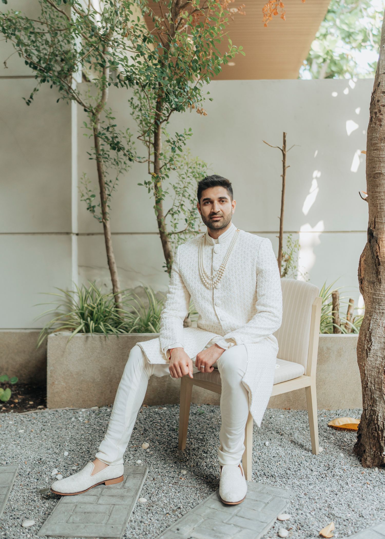 Five stylish photographs of someone wearing an elegant all-white outfit sitting in a modern minimal backyard setting.