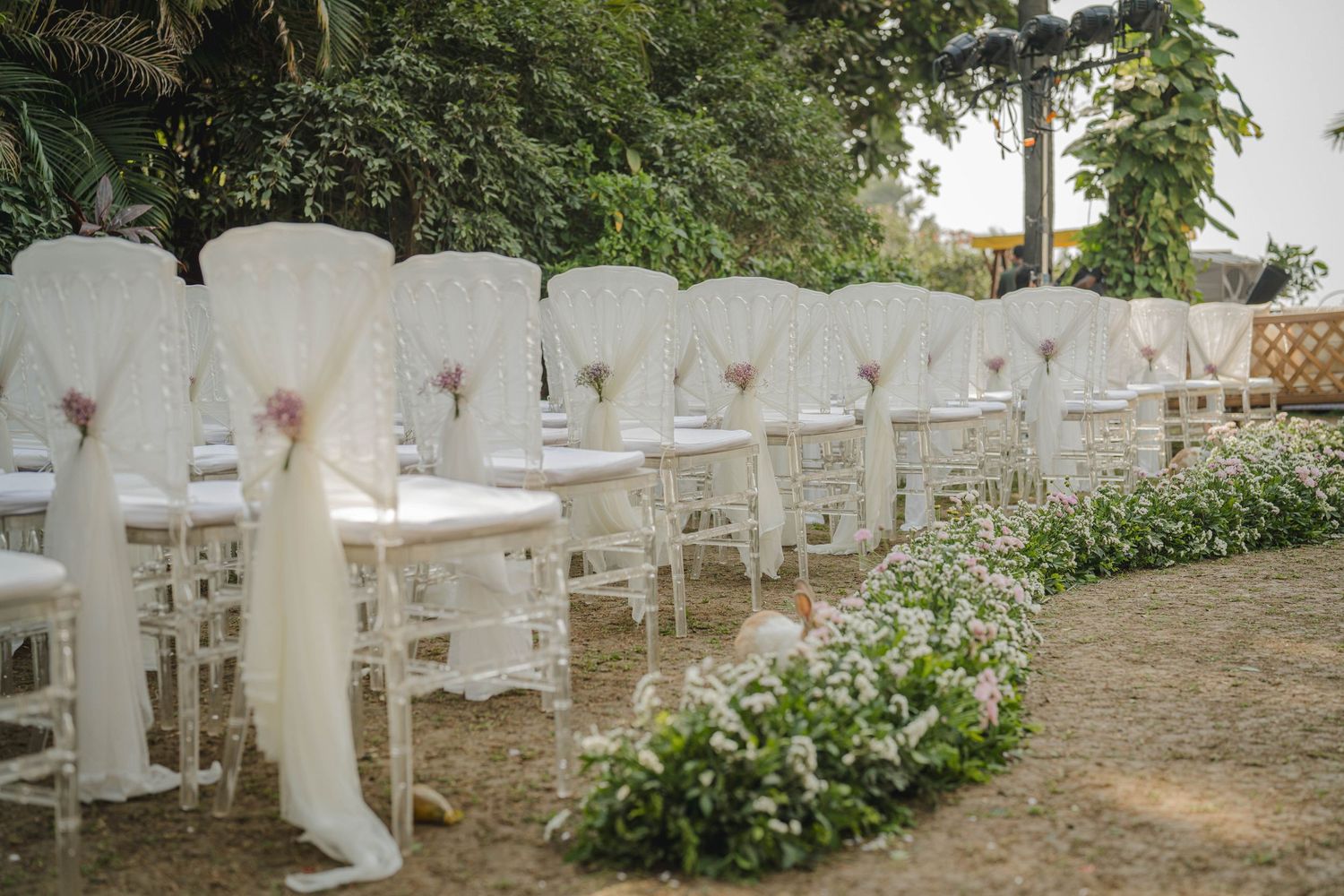 White boots lined up along a stone wall with flowering shrubs and plants in the background.