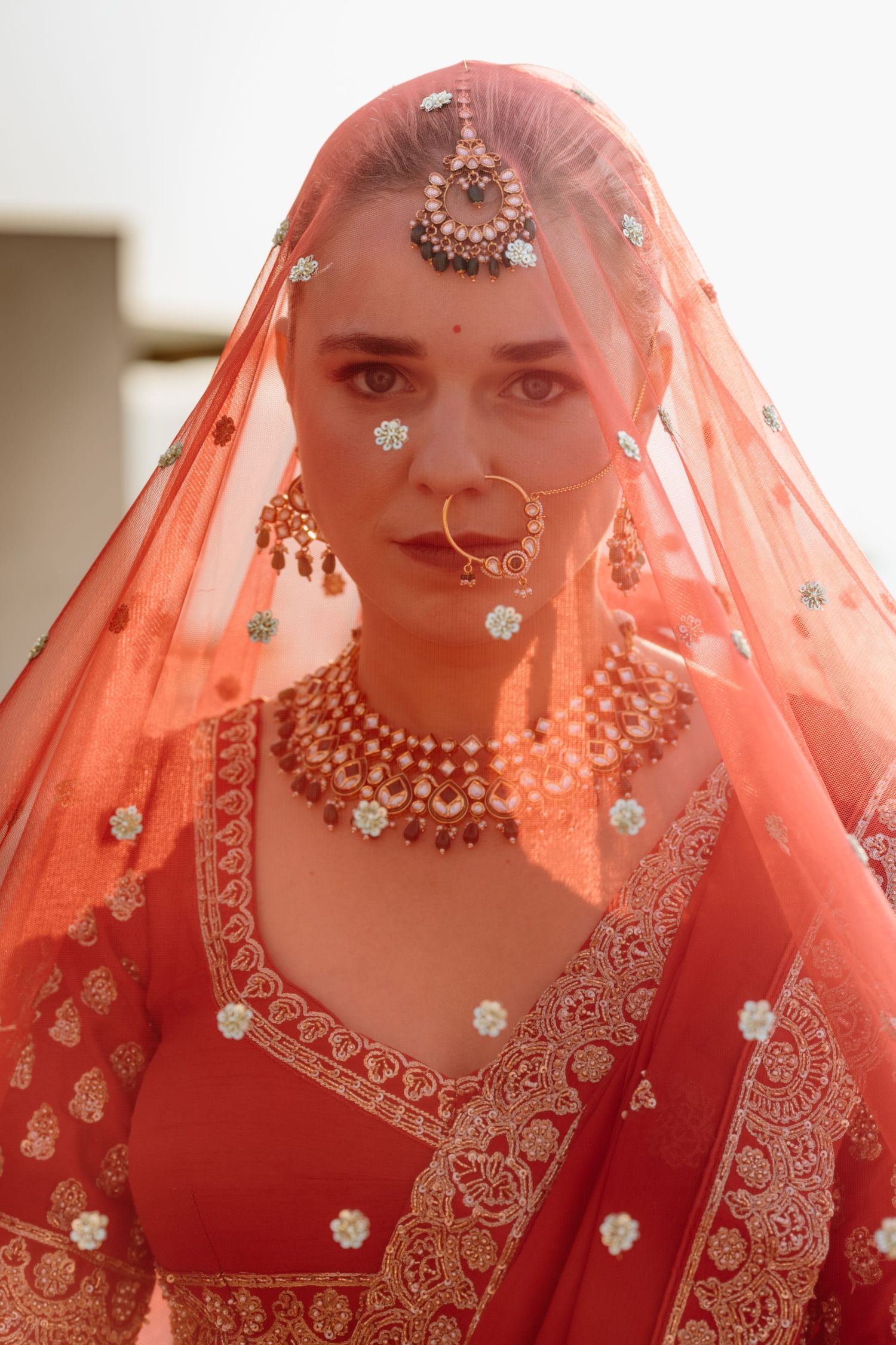 Traditional Indian bridal portrait with coral veil and ornate jewelry.