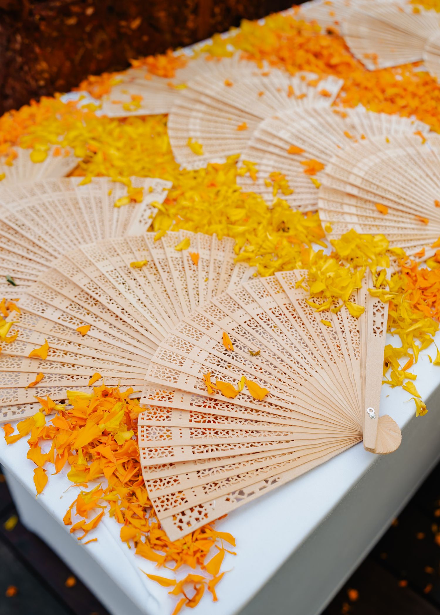 Decorative paper fans arranged on white surface with scattered yellow and orange flower petals.