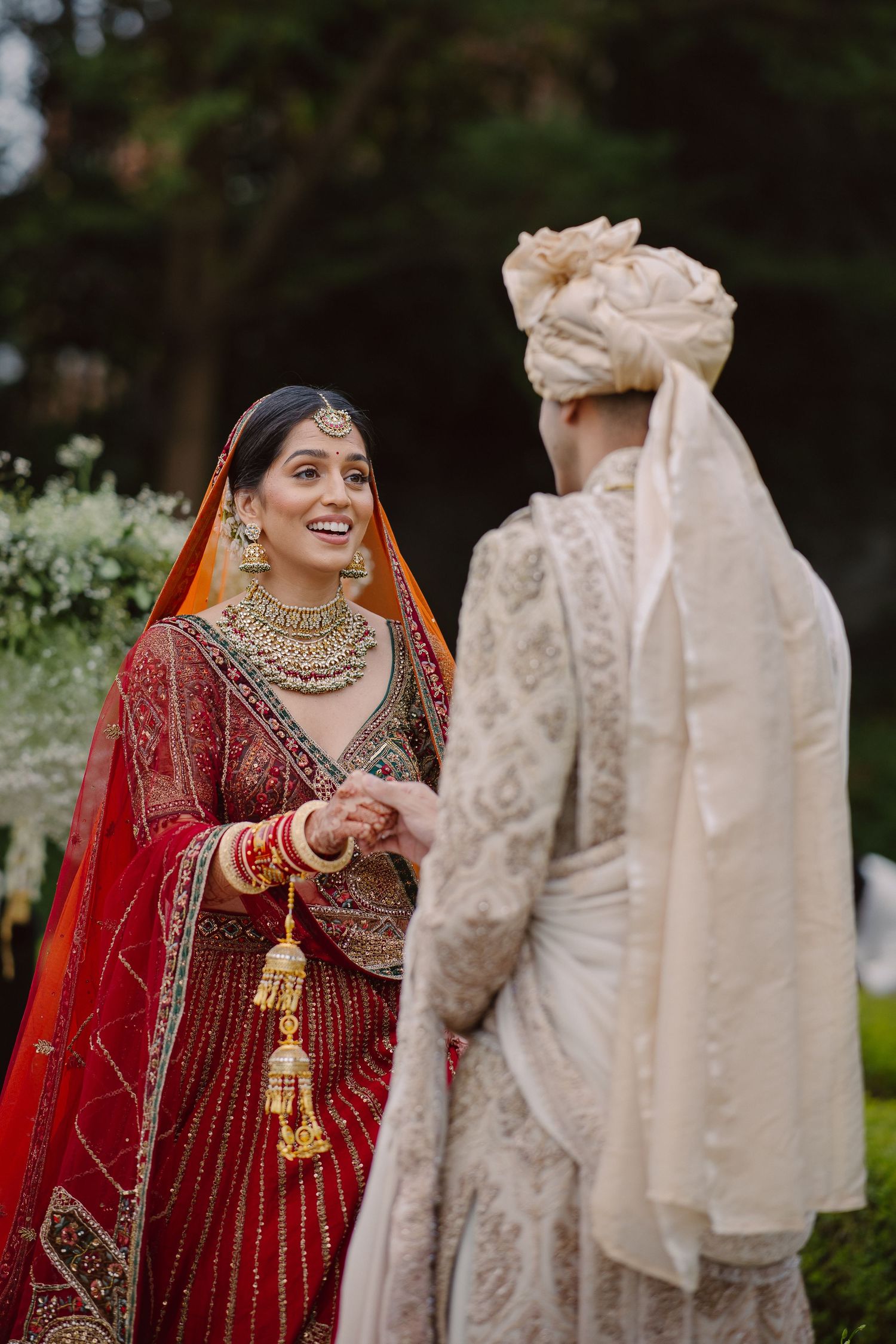 Bride in traditional red Indian wedding attire shares candid moments with guests in cream outfits.