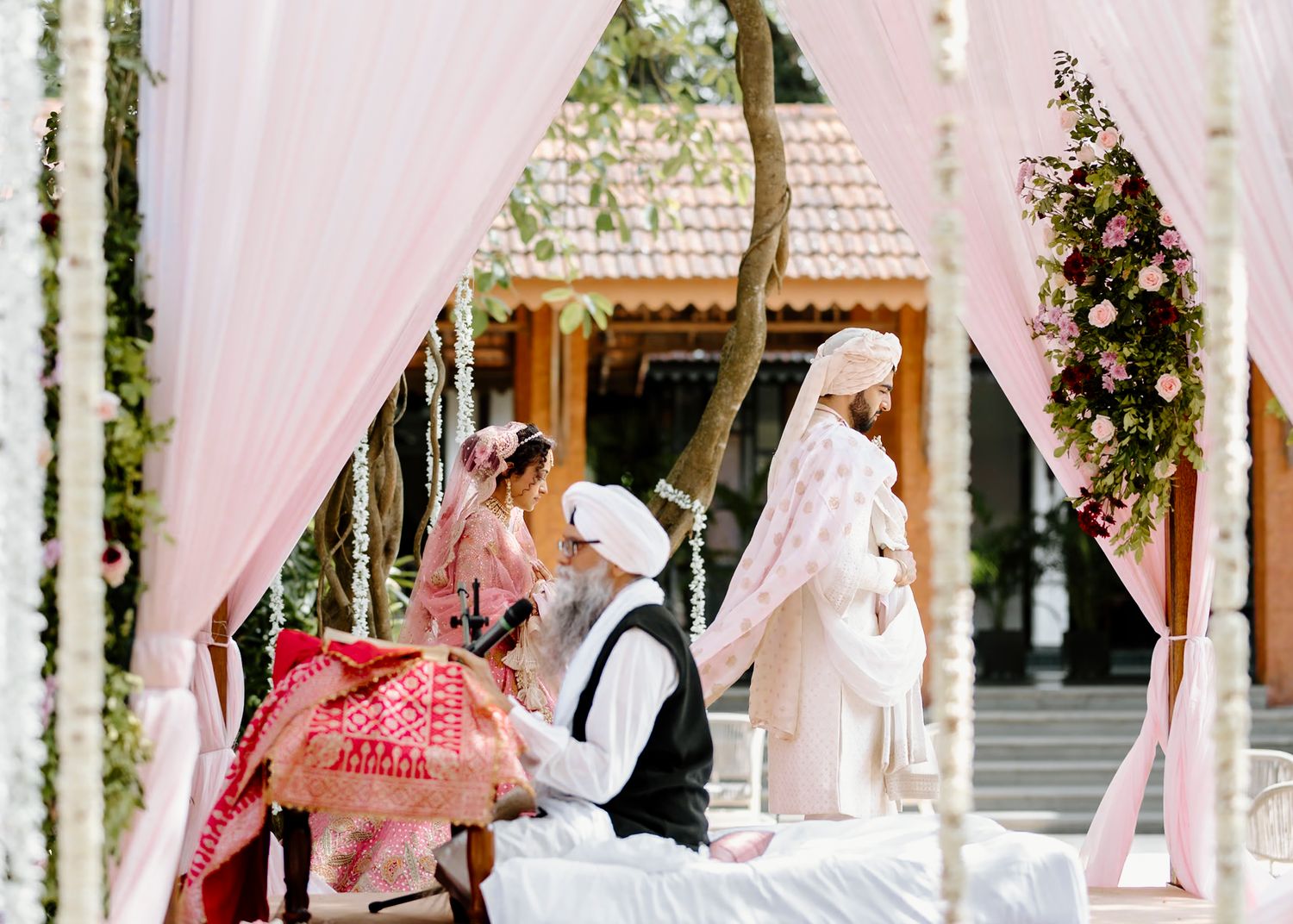 Elegant wedding ceremony setup with pink drapes and floral decorations in an outdoor garden setting.