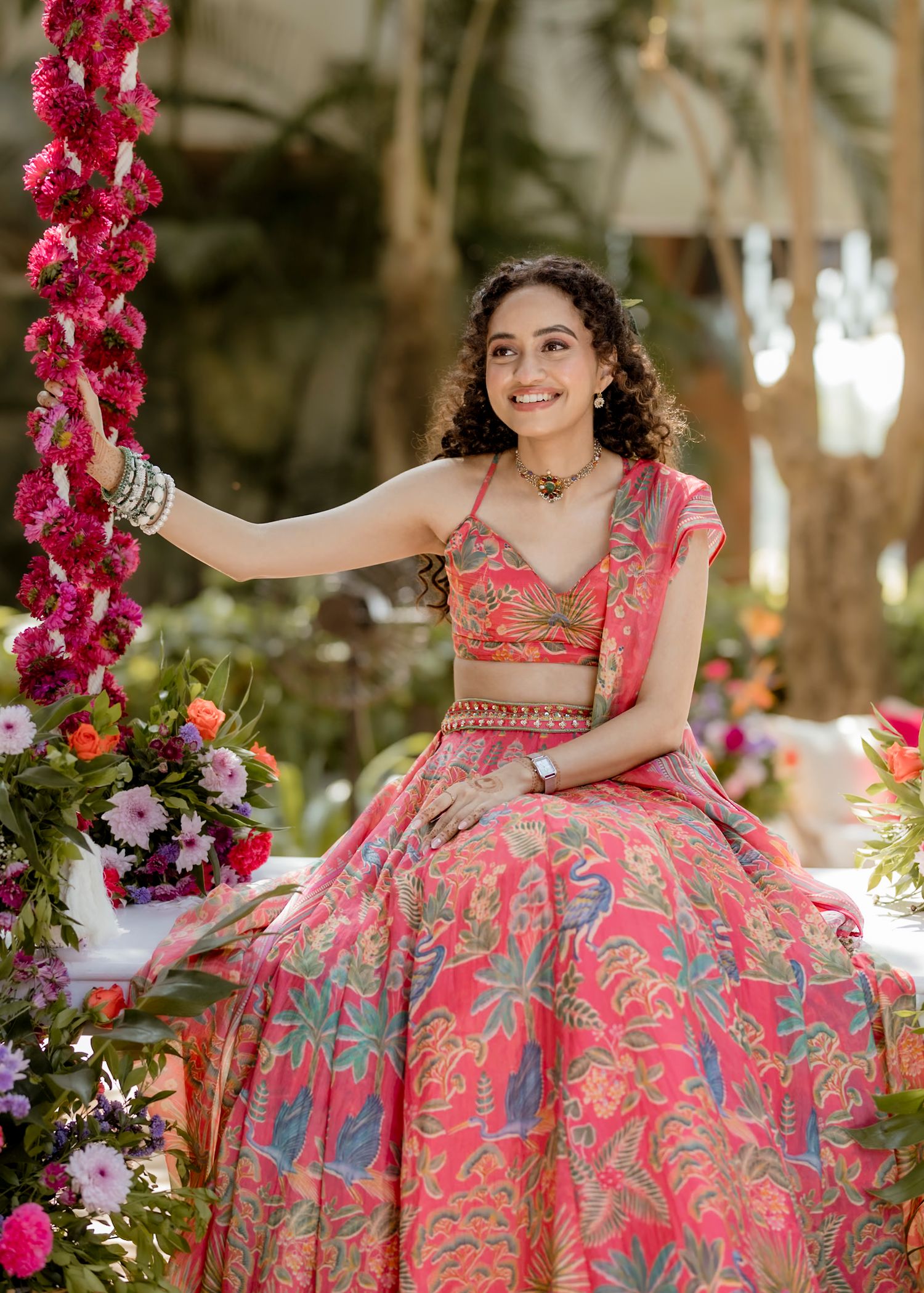 Ornate pink and silver lehenga with floral embroidery displayed in a garden setting with bright pink floral decorations.