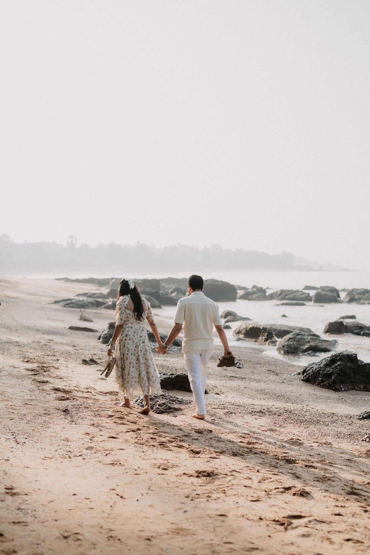 A couple walks hand in hand along a misty rocky beach during a romantic seaside stroll.