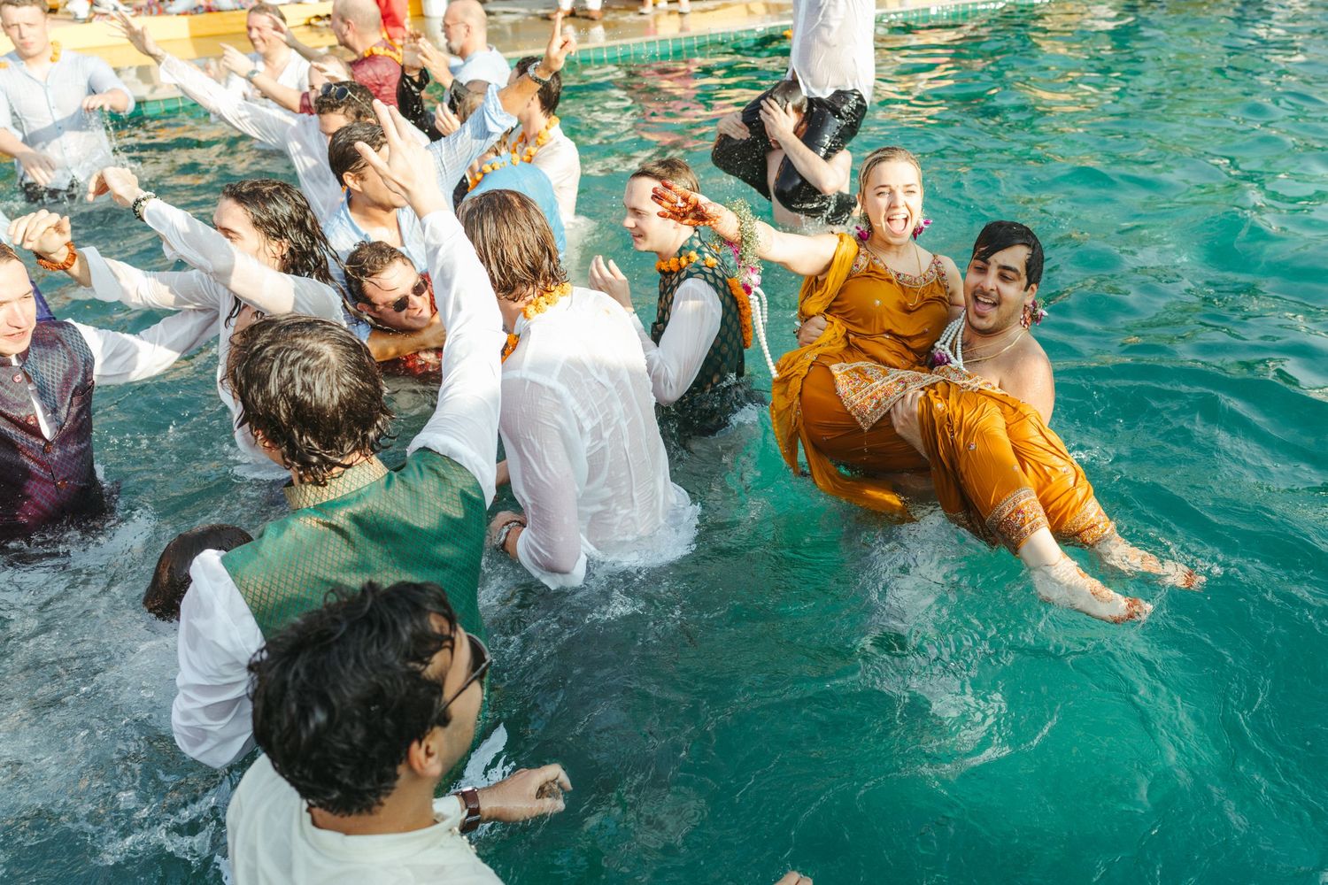 Group of people in colorful attire joyfully splashing in a turquoise pool during a festive celebration.