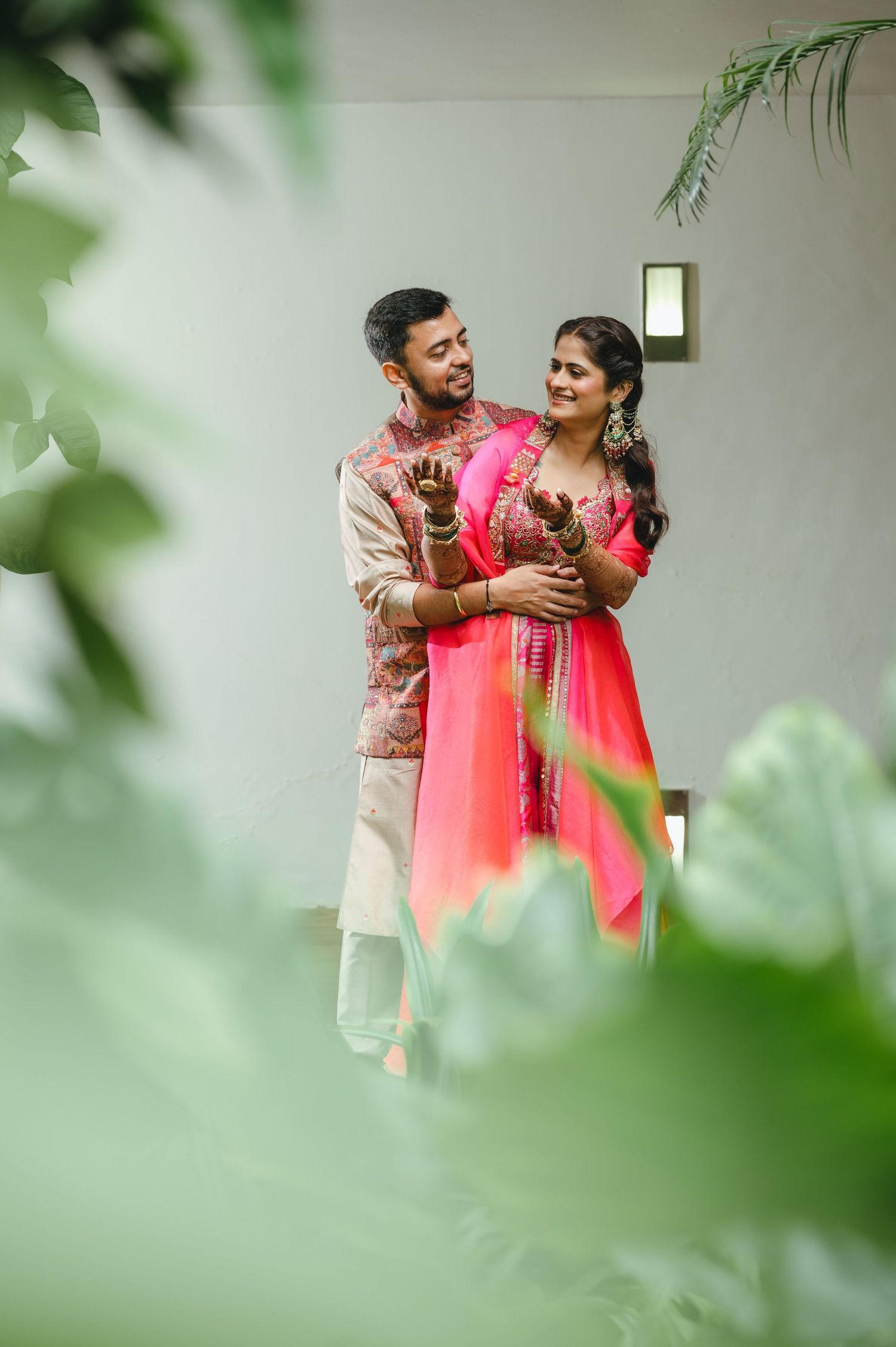 Indian couple in traditional attire embracing outdoors, bride in pink salwar and groom in embroidered sherwani.
