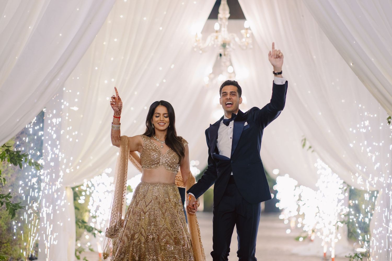 Wedding celebration under a white draped canopy with dramatic lighting and sparkler effects.