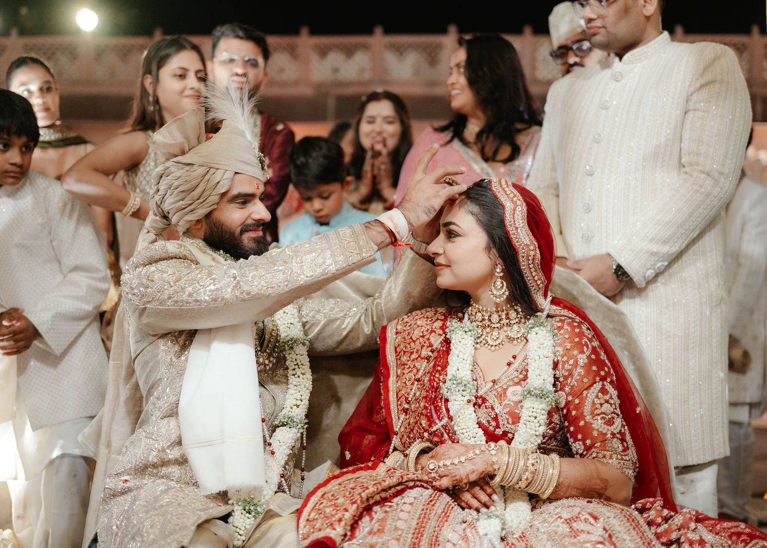 Groom applying sindoor to bride in traditional red bridal lehenga during Indian wedding ceremony.