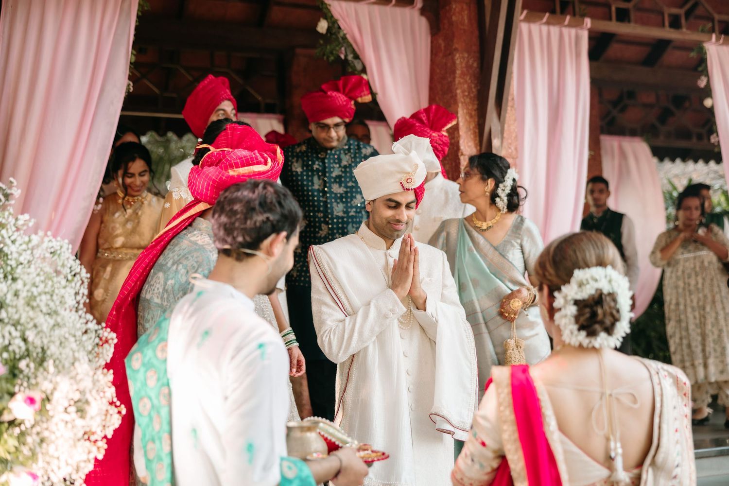 A traditional Indian wedding ceremony with guests in white and red attire seated under a decorated mandap.